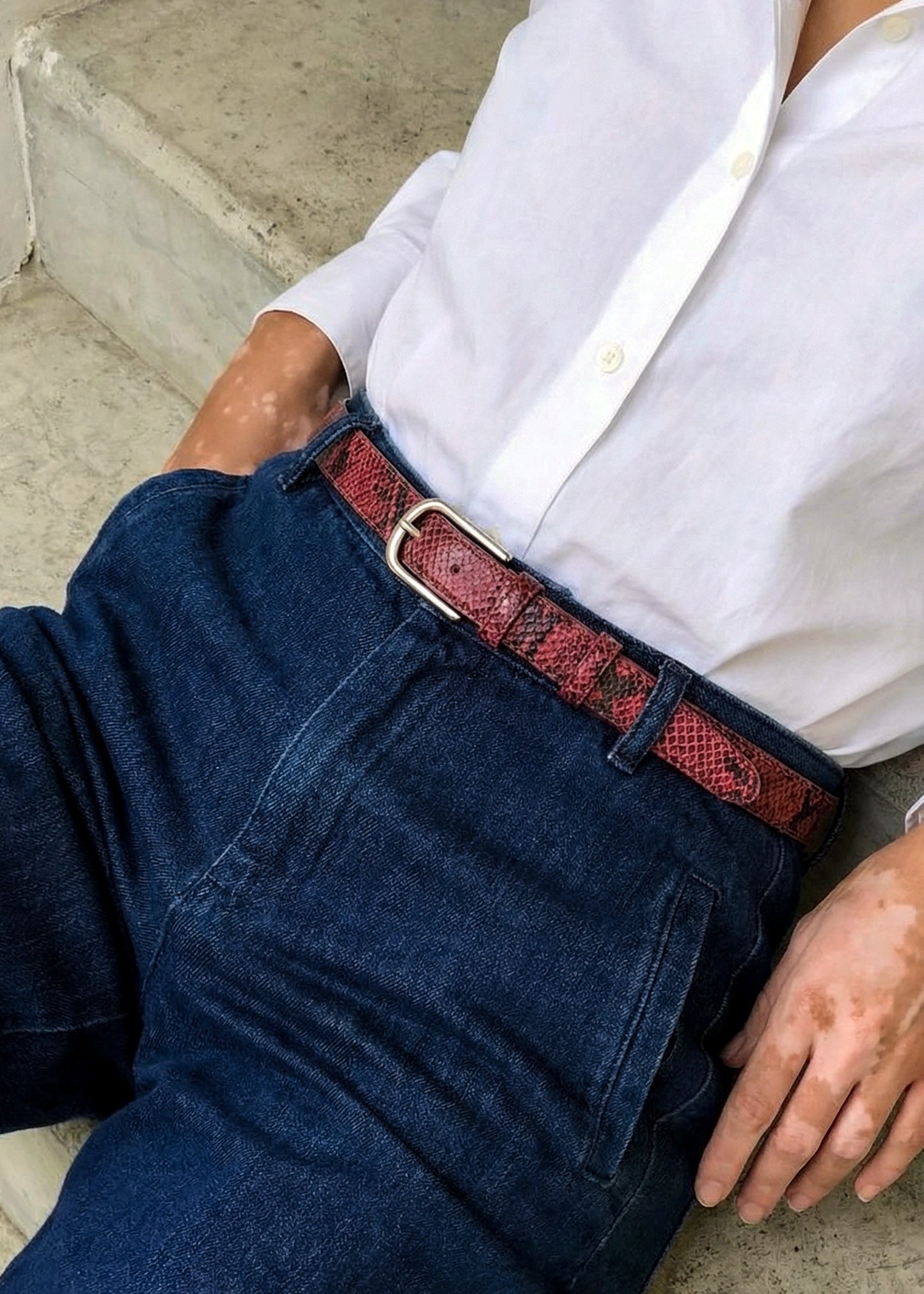 Pink snakeskin belt with a silver buckle, styled on dark blue denim with a white button-down shirt.